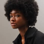 A woman with an afro hairstyle is seated, exuding confidence and style in a relaxed posture.